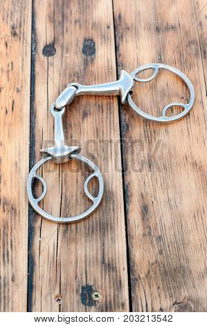 Steel horse snaffle-bit on wooden background. Outdoors close-up.