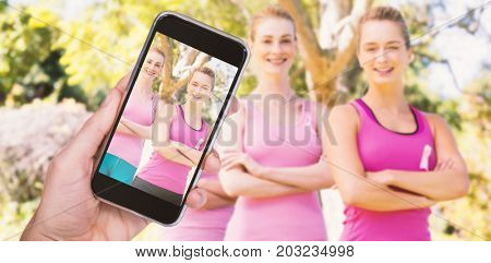 Hand holding mobile phone against white background against portrait of confident volunteers supporting breast cancer social issue