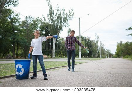 A full-length portrait of a little serious boy and a slovenly young man on a blurred natural background. A child showing thumb down to a guy throwing a bottle in the middle of the road. Copy space.