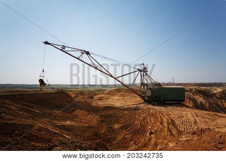 An industrial moving machine in the foundation pit. Yellow mobile crane working in the sandy quarry. Industry equipment on a blue sky background. Technology, cargo, commerce, transport concept.