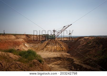 An industrial moving machine in the foundation pit. Yellow mobile crane working in the sandy quarry. Industry equipment on a blue sky background. Technology, cargo, commerce, transport concept.