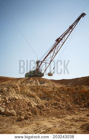 Yellow mobile crane working in the sandy quarry. An industrial moving machine in the foundation pit. Industry equipment on a blue sky background. Technology, cargo, commerce, transport concept.