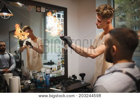 A hairdresser heating the blade of fashioned straight razor under a stream of fire for smoother shaving on a barbershop background. A barber preparing tools for traditional beard shave in the salon.