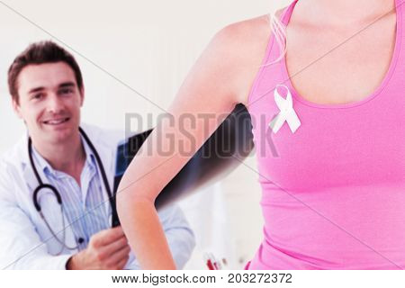 Mid section of woman wearing ribbon for breast cancer awareness against portrait of doctor holding xray