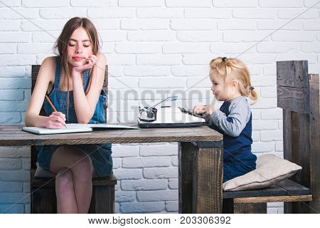 Girl and child sitting at table. Young woman writing in notebook. Kid typing on vintage typewriter. Innovation and archaism. Study and learning concept