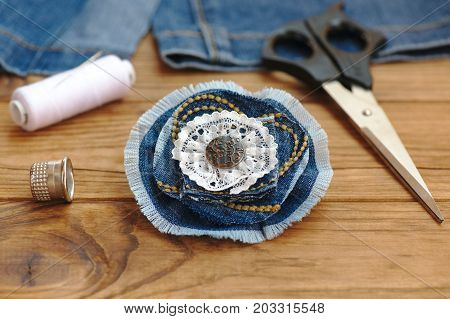 Blue flower brooch or hair accessory. Scissors, thread, thimble, needle, old jeans on a wooden table. Recycle jeans projects. What to do with old blue jeans. Cheap crafts to make. Closeup