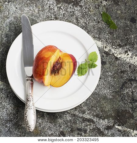 Juicy fresh nectarine on a white plate with a vintage silver knife on a gray stone background. Top View
