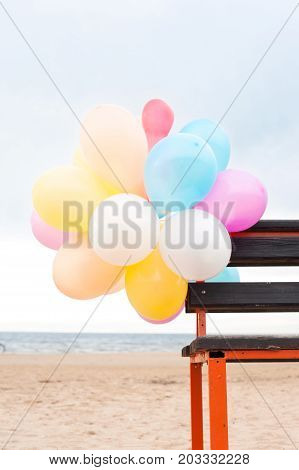 Bunch of multicolored air balloons attached to wooden bench on blue sky backgorund. Outdoors.