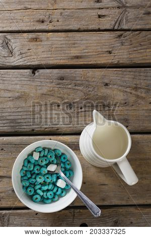 Bowl of froot loops and marshmallow with milk jug on wooden table