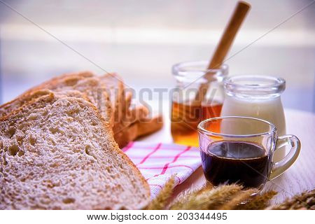 Sliced crusty country style round organic french bread with coffee and honey bee with milk on the table.
