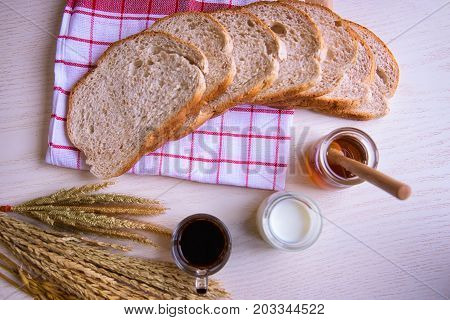 Sliced crusty country style round organic french bread with coffee and honey bee with milk on the table.