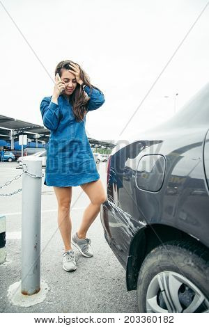 sad woman standing near car with scratch on parking and talking by the phone