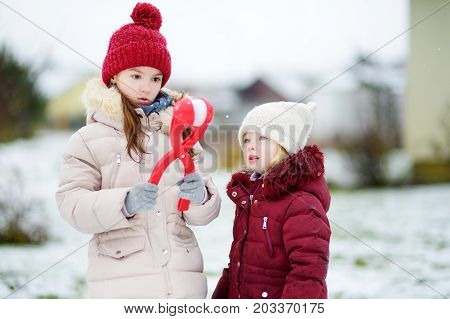 Two Adorable Little Girls Having Fun With Snowball Maker In Beautiful Winter Park. Beautiful Sisters
