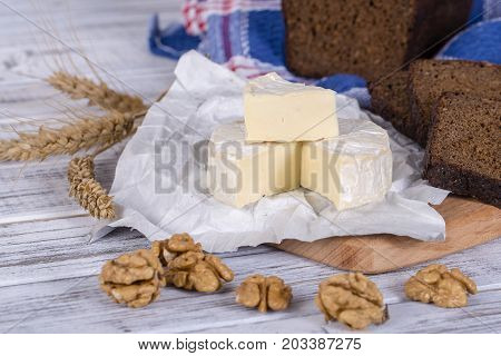 Brie cheese or camembert cheese. Fresh Brie cheese and slice on a wooden board with walnuts and black bread slice. Italian or French cheese. Close up