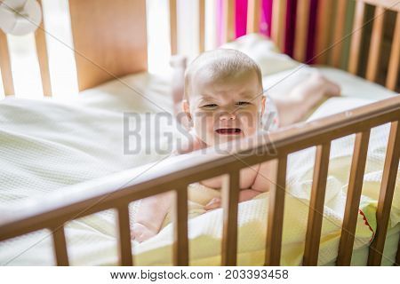 A Close-up portrait of a crying cute baby in the crib at home