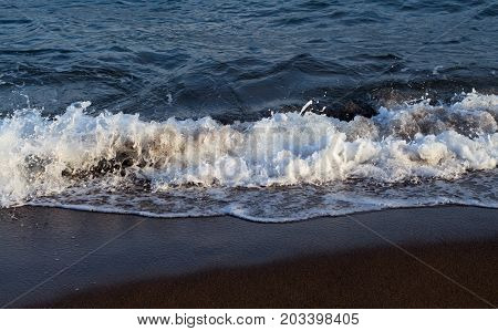 Blue sea water tide on dark volcanic beach. Relaxing sea wave surf over seashore. Coastal seaview. Seascape for summer vacation. Exotic island seaside banner. Sea close-up. Seawater splash on beach