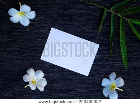 Flat lay with white paper and green bamboo. Blank white postcard mockup. Tropical travel. Exotic flower flat lay. White frangipani flowers. Green bamboo leaf. Tropic natural banner. Wedding invitation