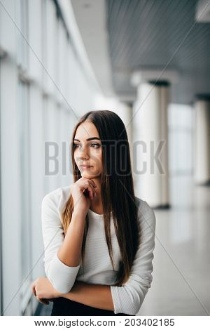 Attractive Young Businesswoman Portrait With Hands On Chin Near Office Windows
