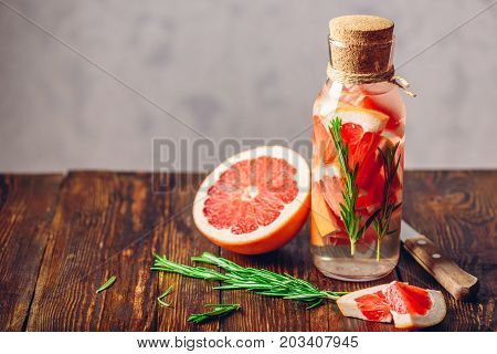 Cleansing Water with Sliced Raw Grapefruit and Fresh Springs of Rosemary. Ingredients and Knife on Wooden Table. Copy Space on the Laft.