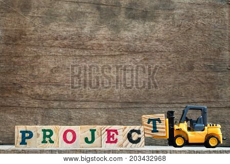 Toy plastic forklift hold block T to compose and fulfill wording project on wood background
