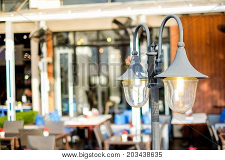 The vintage street lamp (lantern) shine near the outdoor restaurant for background or texture.