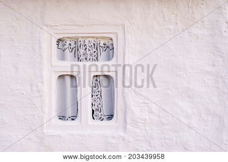 Wall from the whitewashed clay of an old house for habitation with a thatched roof and rounded windows in rectangular black frames with shutters