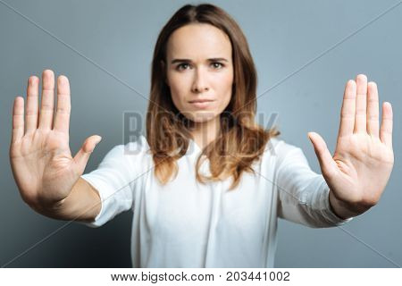 Serious look. Nice serious young woman standing behind the glass screen and pressing her palms to it while looking at you