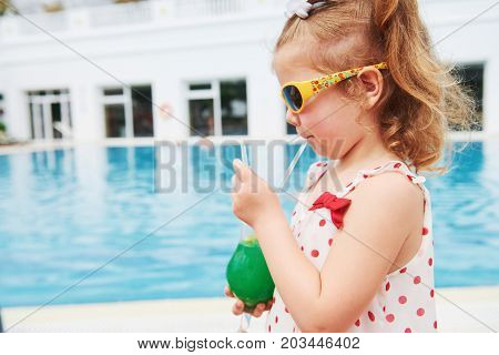 Cute little blonde at the pool and holding achild's cocktail .