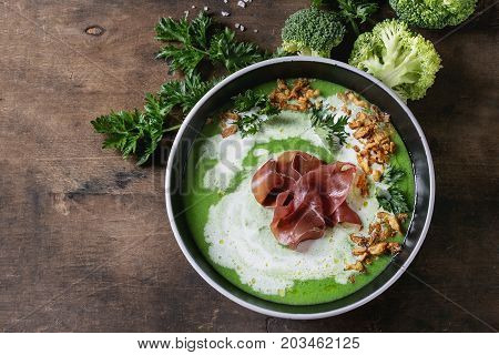 Vegetable broccoli cream soup served in black bowl with italian bresaola ham cream, fried onion, fresh parsley and broccoli over old wooden background. Top view with space. Healthy eating.