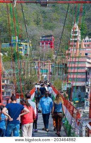 Rishikesh, India - March 10, 2017: People Crossing The Ganges River On The Suspension Footbridge At