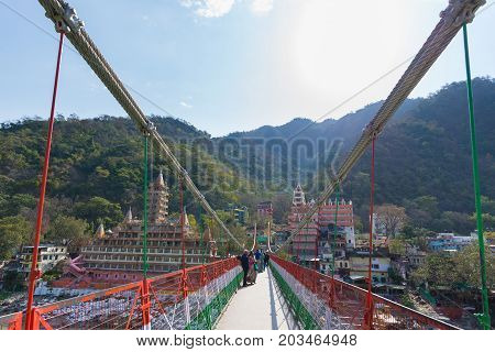 Rishikesh, India - March 10, 2017: People Crossing The Ganges River On The Suspension Footbridge At
