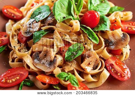 Home made vegan pasta with mushrooms tomatoes basil peppers and aubergines - served on plate at wooden table background; close up.