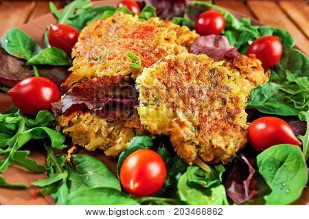Homemade veg burgers from potatoes and lentils served on a plate with tomatoes and green salad on a wooden background; close up.