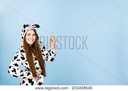 Happy teenage girl in funny nightclothes pajamas cartoon style pointing up with positive smiling face expression studio shot on blue. Advertisement concept