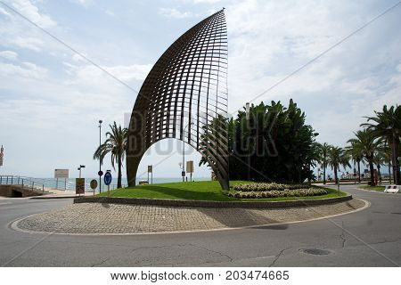 CAMBRILS, SPAIN - AUG 27th, 2017: Modern sculpture A tota vela, a round about and the main street promenade in the port area with Cambrils sign in the background.