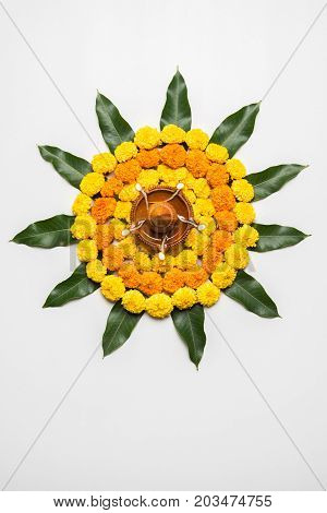 flower rangoli for Diwali or pongal or onam made using marigold or zendu flowers and red rose petals over white background with diwali diya in the middle, selective focus