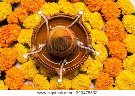 flower rangoli for Diwali or pongal or onam made using marigold or zendu flowers and red rose petals over white background with diwali diya in the middle, selective focus
