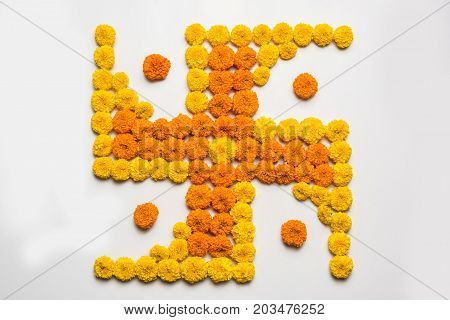 stock photo of hindu auspicious symbol called Swastika made using marigold flower or zendu or genda phool, Flower rangoli in the shape of Swastika for diwali/pongal/onam over white background