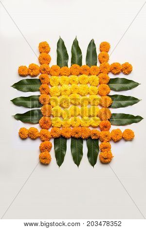 flower rangoli for Diwali or pongal or onam made using marigold or zendu flowers and red rose petals over white background with diwali diya in the middle, selective focus
