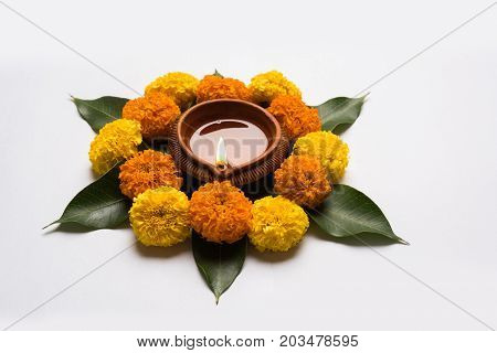 flower rangoli for Diwali or pongal or onam made using marigold or zendu flowers and red rose petals over white background with diwali diya in the middle, selective focus