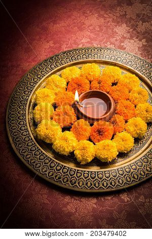 flower rangoli for Diwali or pongal or onam made using marigold or zendu flowers and red rose petals over white background with diwali diya in the middle, selective focus