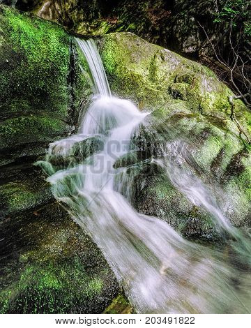 A small water fall spills along moss covered rocks. Water Fall photograph was taken in the summer when there was not much water flowing int he brook.