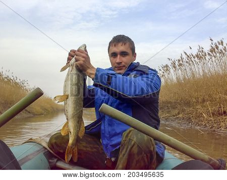 The Fisherman Caught A Pike And Held It In His Hands Behind The Gills. Fisherman In A Boat. Fishing