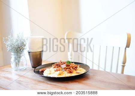 The beautiful houseplant in clear flowerpot tissue in black box spaghetti carbonara with bacon and mushroom sauce set on wooden table and white chair food background or texture -interiors concept.