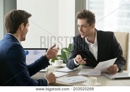 Two successful businessmen discussing company financial strategy, analyzing economic indicators, planning profitability and stock value growth while sitting at desk in office during business meeting