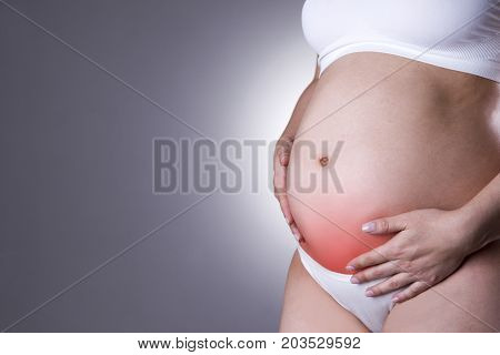 Caucasian pregnant woman in white lingerie with abdominal pain on gray studio background. Pregnancy concept