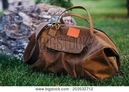 Retro brown shoes and man leather bag in bright colorful summer grass in the park.