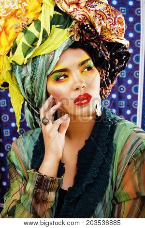 beauty bright woman with creative bright make up, many shawls on head like cubian, ethno look closeup