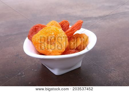 Delicious dried organic apricots in bowl isolated on stone table