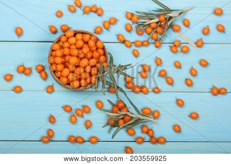 Sea buckthorn. Ripe fresh berries in bowl on blue wooden background. Top view.
